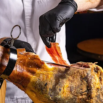 Un chef en gants noirs tranche de fines lamelles de jambon cru salé à Bourges dans le Cher 18