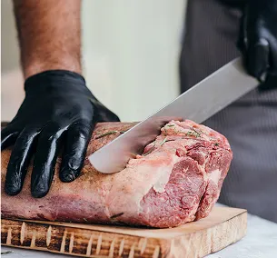 Un boucher ganté de noir tranche un gros morceau de viande sur une planche à découper à Bourges dans le Cher 18
