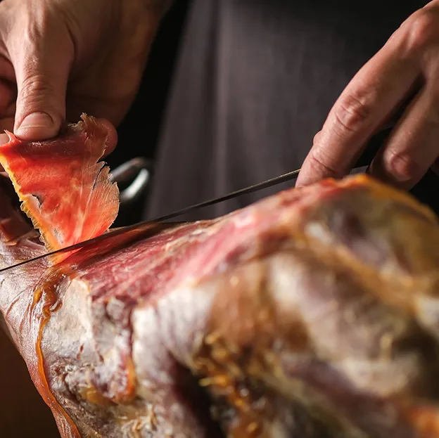 Mains tranchant finement du jambon cru avec un couteau, fond sombre à Bourges dans le Cher 18